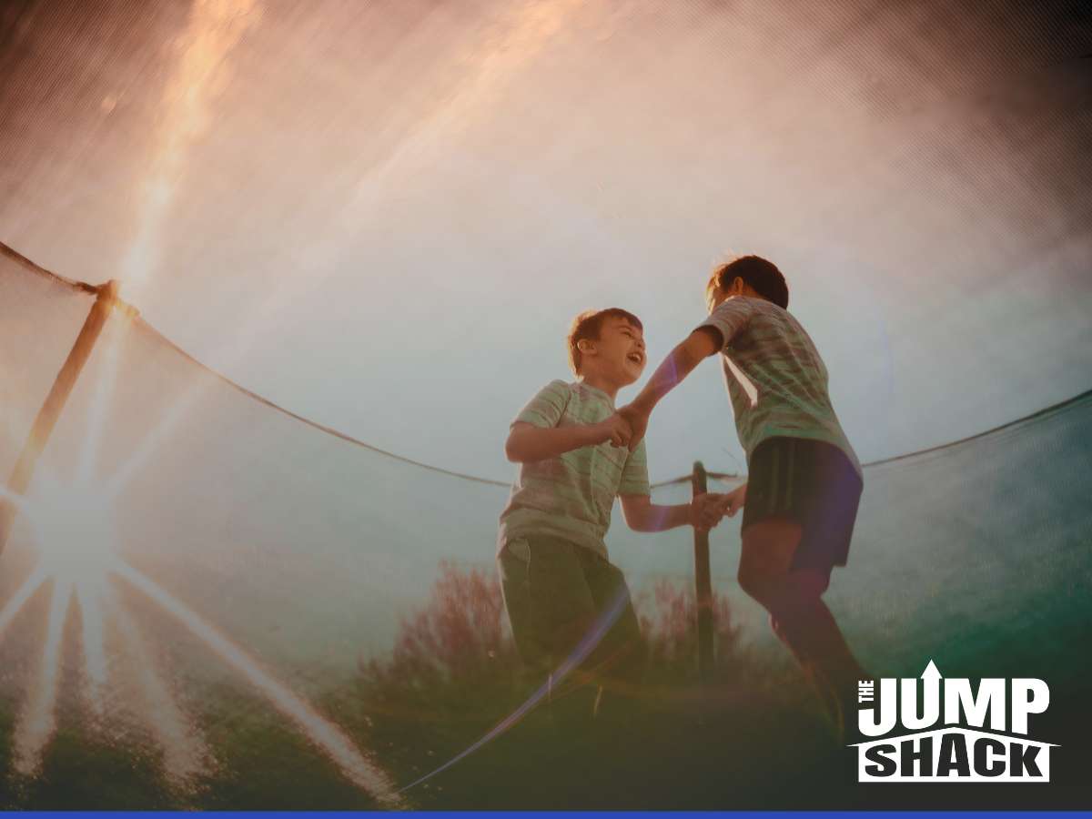 Two kids laughing and jumping on an in-ground trampoline at sunset