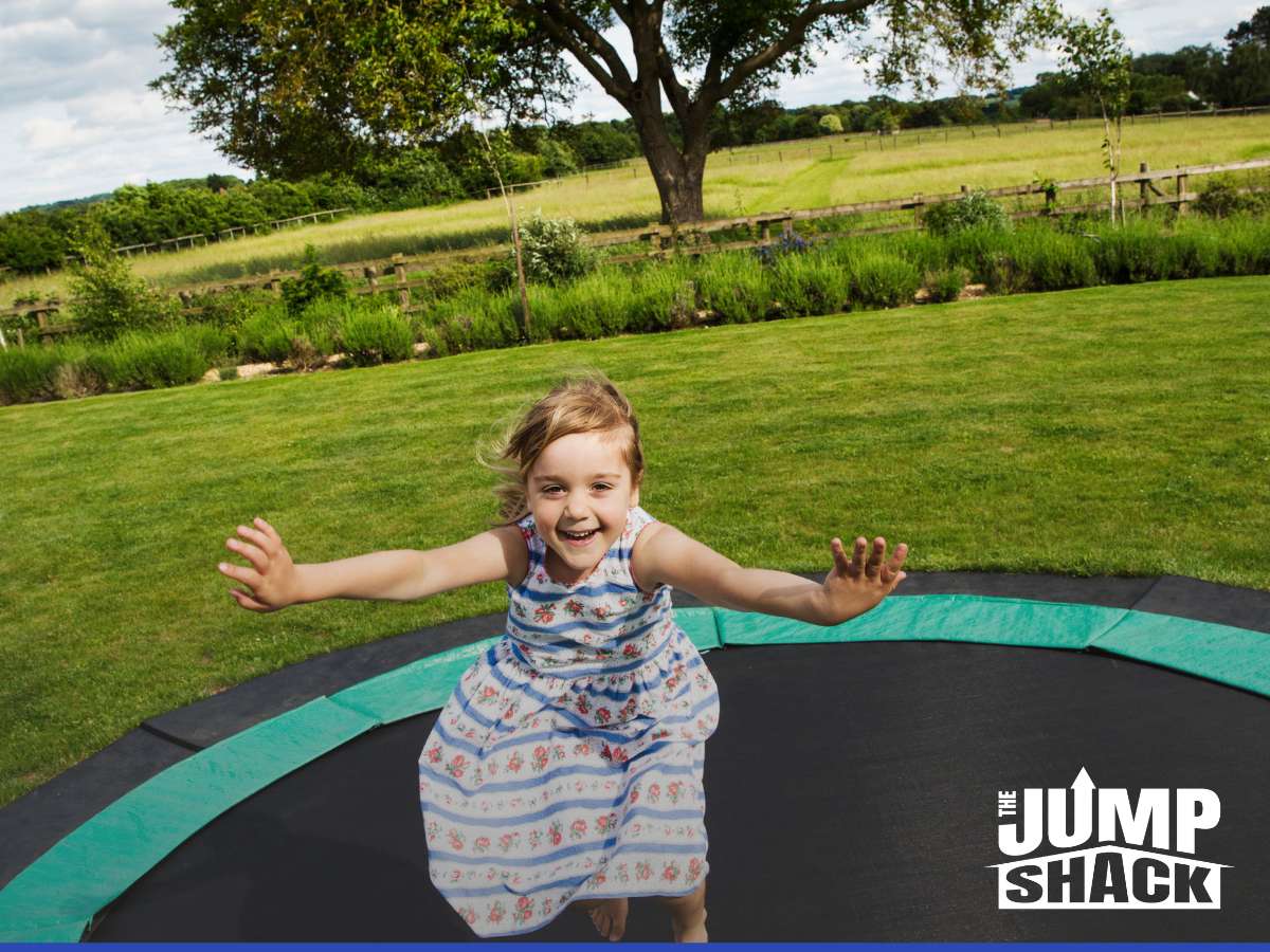 oyful child playing on one of Arizona in-ground trampolines in a sunny backyard, with 'The Jump Shack' logo.