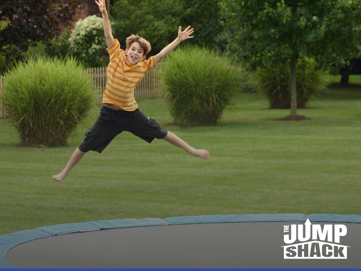 Boy joyfully jumping on an in-ground trampoline in a backyard