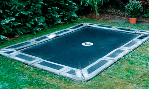 Rectangular in-ground trampoline set flush with the lawn in a landscaped backyard