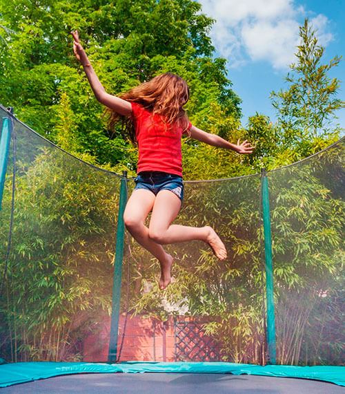 Child jumping on an in-ground trampoline with a safety net enclosure